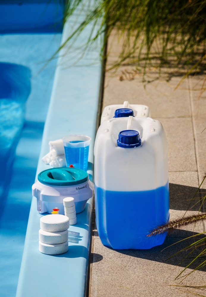 Chlore et Entretien Piscine : Produits pour une eau claire. Produits d'entretien de piscine : galets de chlore, doseur et jerrycans de désinfectant liquide bleu près du bord du bassin.