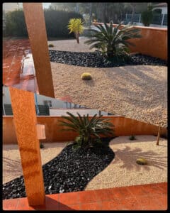 Aménagement de jardin sec. Contraste fort entre un chemin de gravier noir et des galets beiges, accentué par des cycas et cactus.
